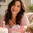 Happy woman celebrating her birthday at home with a cake, flowers, and birthday gifts in a bright sunlit room.