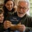 Grandfather smiling as he opens a Father's Day card while his grandchildren gather around him, celebrating together at home.