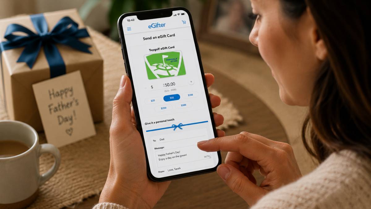 Woman personalizing a Topgolf eGift card on her smartphone for Father's Day, adding a message while preparing a thoughtful gift for a new dad.