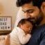 New father holding a sleeping newborn in a cozy living room on Father's Day, with a "Best Dad Ever" sign in the background.