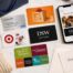 Flat lay of a thoughtfully arranged collection of physical and digital gift cards, a smartphone displaying a personalized digital gift card, stationery, ribbon, and gift packaging, representing creative and flexible ways to give gift cards.