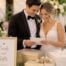 Newly married couple reading a wedding card beside a gift table at their reception
