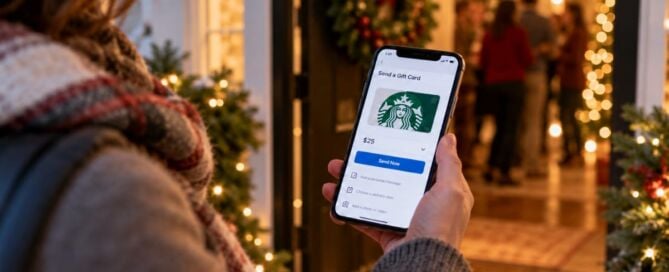 Person holding a smartphone displaying a $25 Starbucks digital gift card outside a festive holiday gathering.